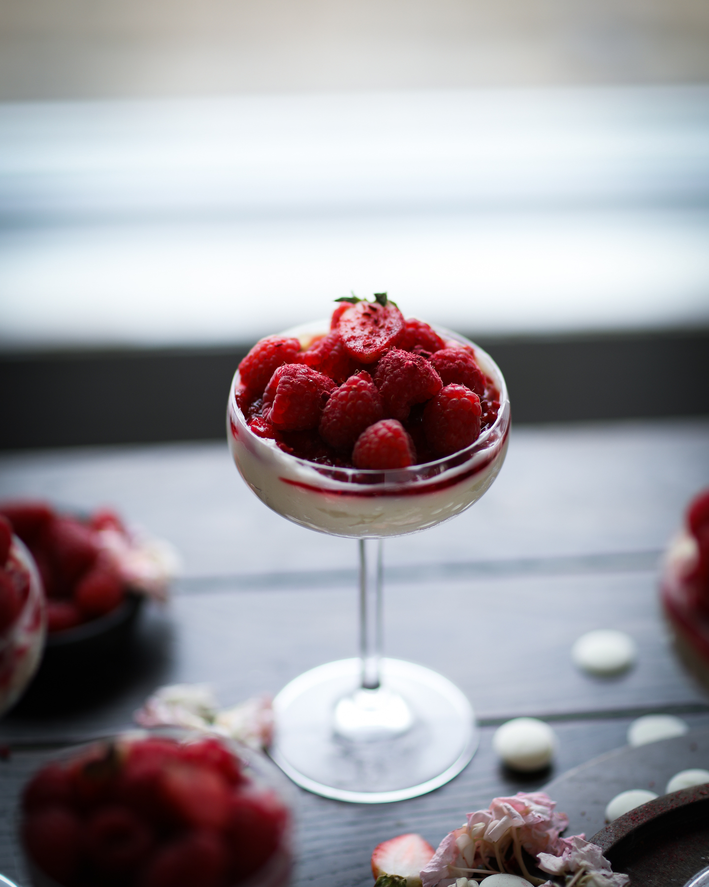 Coupe glass filled with cheesecake filling topped with berries and crushed freeze dried berries. Photo is shot with backlighting. 