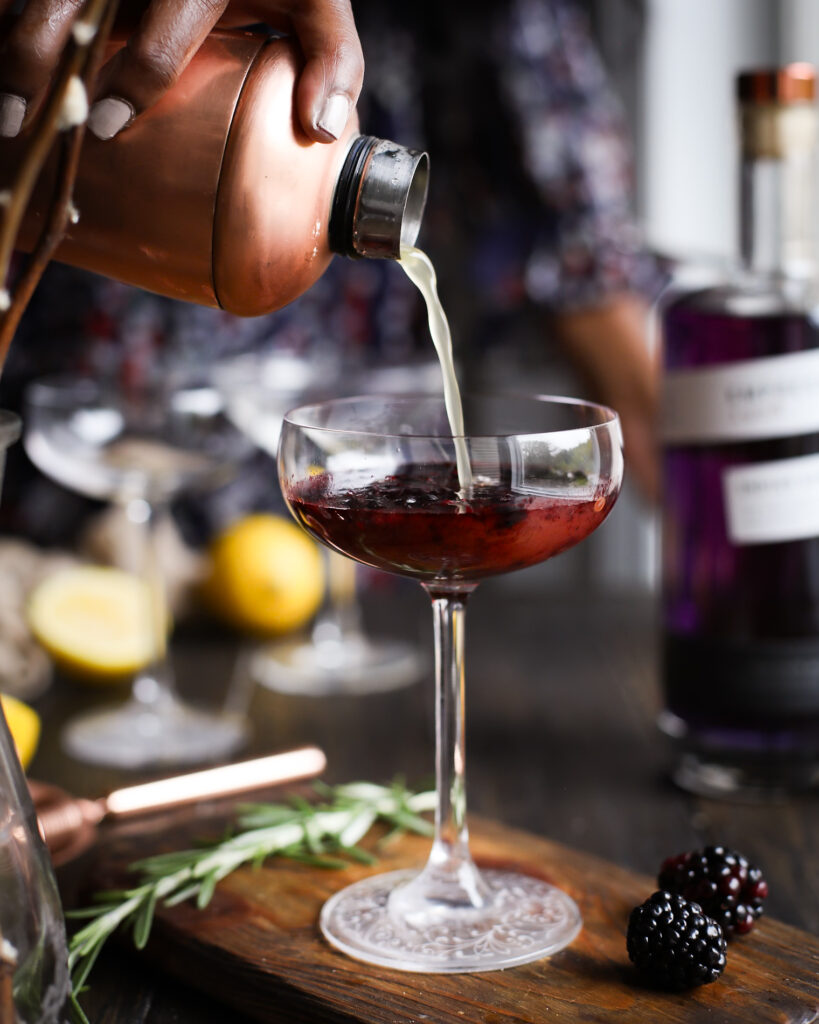 Pouring citrus juice into a couple glass of muddled blackberries.