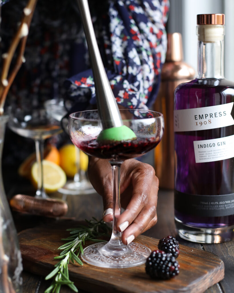 Muddling blackberries in a coupe glass.